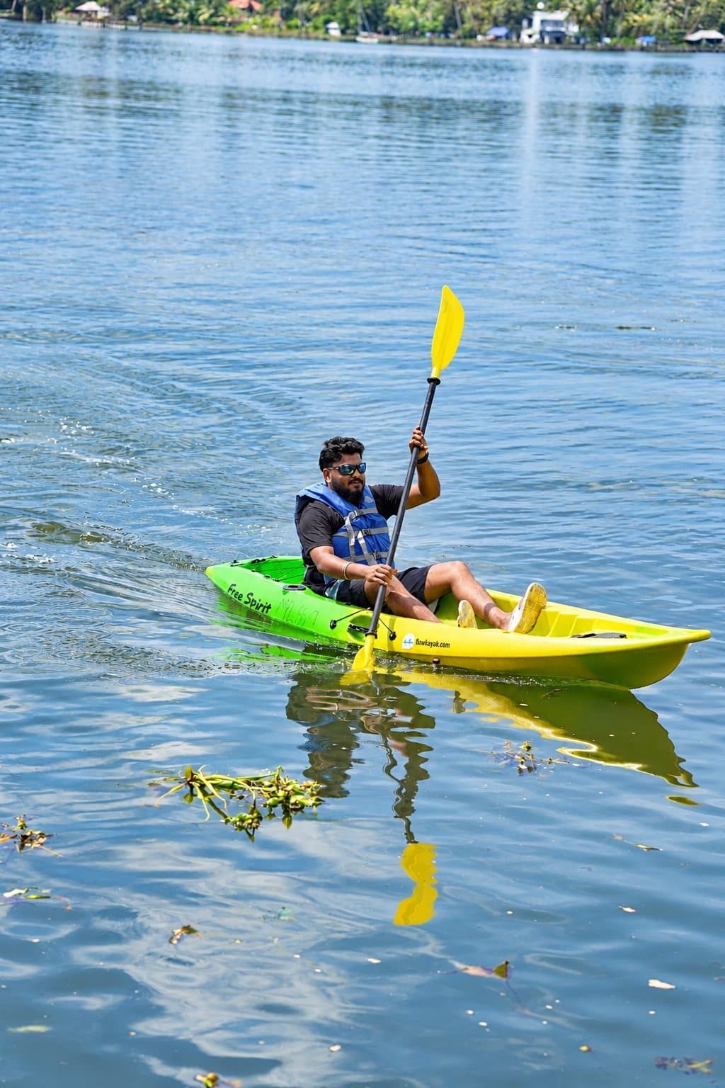 A paddler in a blue buoyancy aid and sunglasses in a lime-green sit-on-top kayak, reflected in calm water