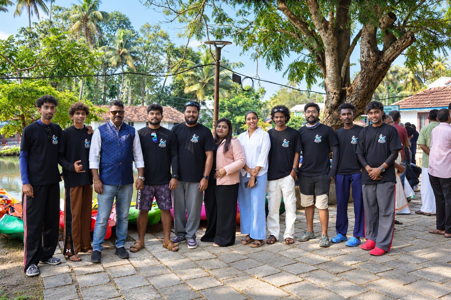 The Bond Safari team, most in black team T-shirts, standing on a paved waterside path with kayaks behind them