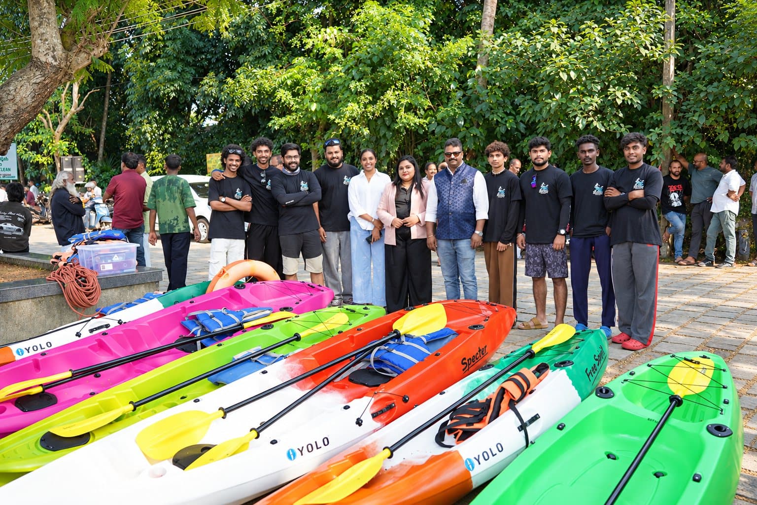 The Bond Safari team, many in Muziris Water Trails T-shirts, standing behind a row of colourful kayaks and yellow paddles under green trees
